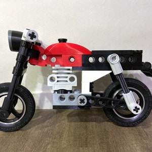 May include: A red, white, and black toy motorcycle made of plastic building blocks. The motorcycle has a black seat, black wheels, and a white headlight.