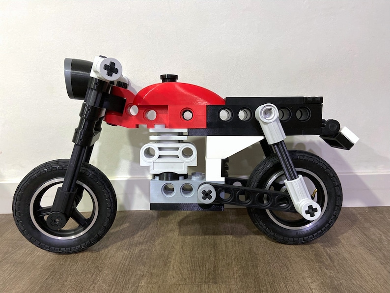 May include: A red, white, and black toy motorcycle made of plastic building blocks. The motorcycle has a black seat, black wheels, and a white headlight.
