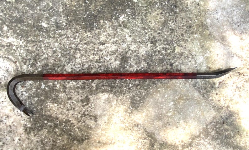 May include: A metal pry bar with a curved end and a pointed tip. The handle is painted a deep red, transitioning to a darker color near the ends. The tool is designed for leverage and prying.