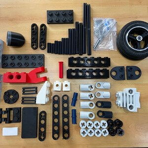 May include: A collection of black, white, red, and blue plastic building blocks. The blocks are various shapes and sizes, including squares, rectangles, and cylinders. There is also a black tire with a silver rim.