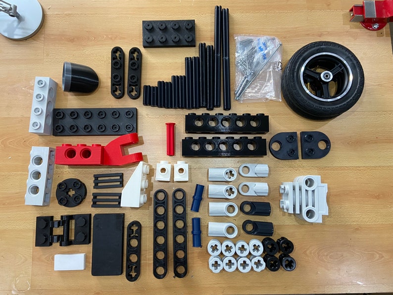 May include: A collection of black, white, red, and blue plastic building blocks. The blocks are various shapes and sizes, including squares, rectangles, and cylinders. There is also a black tire with a silver rim.