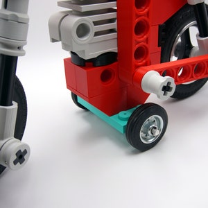 Puede incluir: Una motocicleta de juguete roja, blanca y gris con ruedas negras. La motocicleta tiene un motor detallado y una suspensi&oacute;n delantera.