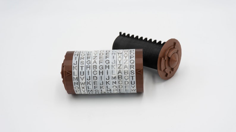 May include: A brown and black rotary encoder with a series of alphabet letters on each ring. The encoder is made of plastic and has a gear on one end.