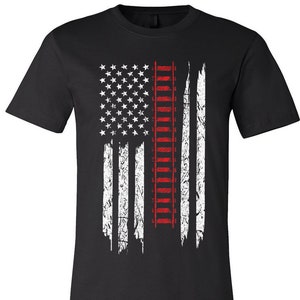 May include: Black unisex short sleeve jersey tee featuring a distressed American flag design. The flag incorporates a red ladder in the center, with white stars and stripes. The shirt's text reads "Unisex Short Sleeve Jersey Tee" and "Black".
