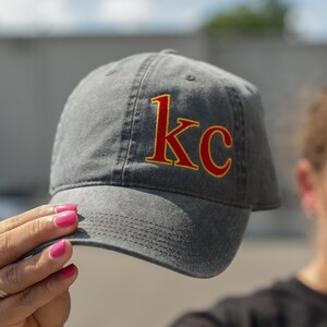 Puede incluir: Una gorra de b&eacute;isbol de algod&oacute;n gris lavado con un "KC" bordado en rojo y amarillo en la parte delantera.