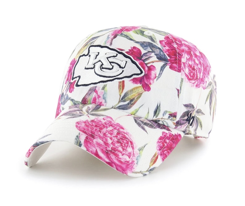 May include: White baseball cap with a floral print featuring pink flowers and green leaves. The front of the cap has a white patch with a black outline and the letters "KC" in black.
