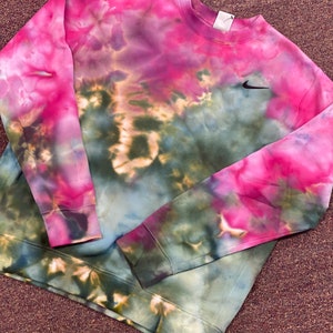 Puede incluir: Una sudadera de color tie-dye en tonos rosa, verde y marr&oacute;n con un logotipo de Nike negro en forma de swoosh en el pecho izquierdo.