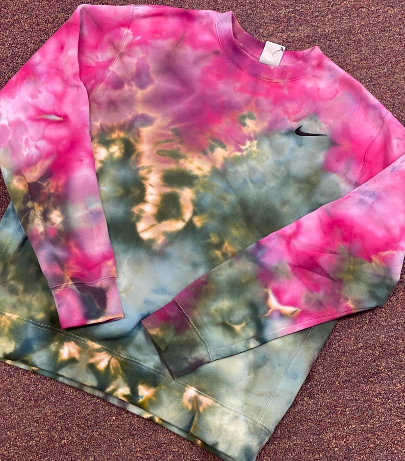 Puede incluir: Una sudadera de color tie-dye en tonos rosa, verde y marr&oacute;n con un logotipo de Nike negro en forma de swoosh en el pecho izquierdo.