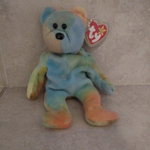 Op de afbeelding: Een blauwe, groene en oranje tie-dye beanie baby beer met zwarte ogen en een rood en wit Ty-label.