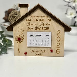 May include: Wooden house-shaped calendar for 2026, featuring a chimney and a dandelion design. The calendar displays the month of January. The text on the house reads "In this house live the best Grandma and Grandpa in the world."