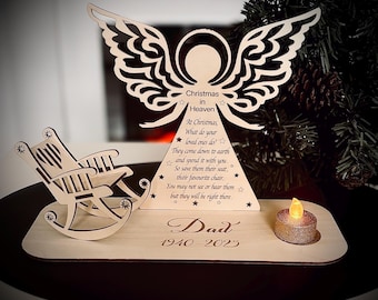 Puede incluir: Memorial navideño de madera con un ángel, una mecedora y una vela. El texto dice "Christmas in Heaven" y "Dad 1940-2023". Una pequeña vela brillante se encuentra en la base de madera.