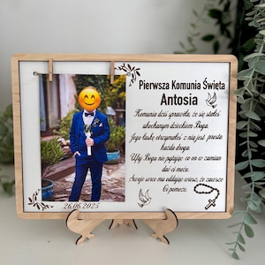 Könnte beinhalten: Ein Holzfotorahmen mit einem Bild einer Person in einem blauen Anzug, einer Fliege und einem Smiley-Gesicht über dem Gesicht. Der Rahmen enthält polnischen Text und das Datum 26.06.2025. Der Rahmen wird von einem Holzständer getragen.