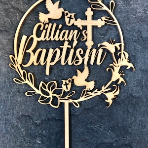 May include: Wooden cake topper with a circular design featuring a cross, doves, flowers, and the text "Cillian's Baptism".