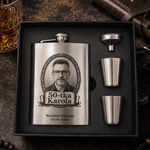 Op de afbeelding: Een roestvrijstalen heupfles cadeau-set in een zwarte doos, inclusief een heupfles met een portret van een man, de tekst 50-tka Karola en de inscriptie Wszystkiego Najlepszego od Gosi i Karola, plus twee kleine metalen bekers en een trechter.