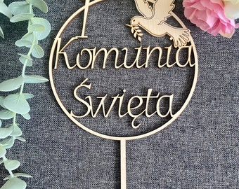 May include: Wooden cake topper with a circle design and the words "I Komunia Swieta" and a dove with an olive branch in its beak.