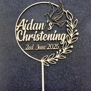 Può includere: Topper per torta in legno con un design circolare che presenta il testo "Aidan's Christening 2nd June 2025" e una colomba con rami di ulivo.