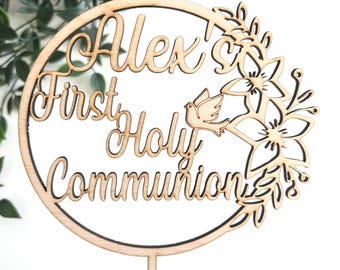 May include: A wooden cake topper with the text "Alex's First Holy Communion" in a circle with a dove and floral design.