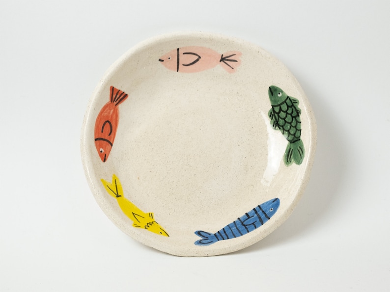The top look of a handmade stoneware fish bowl. IT has five fishes illustrated and handpainted on its inside border. They are all different from each other and small: ocean blue fish, yellow thin fish, red normal fish, pink fish and dark green fish.