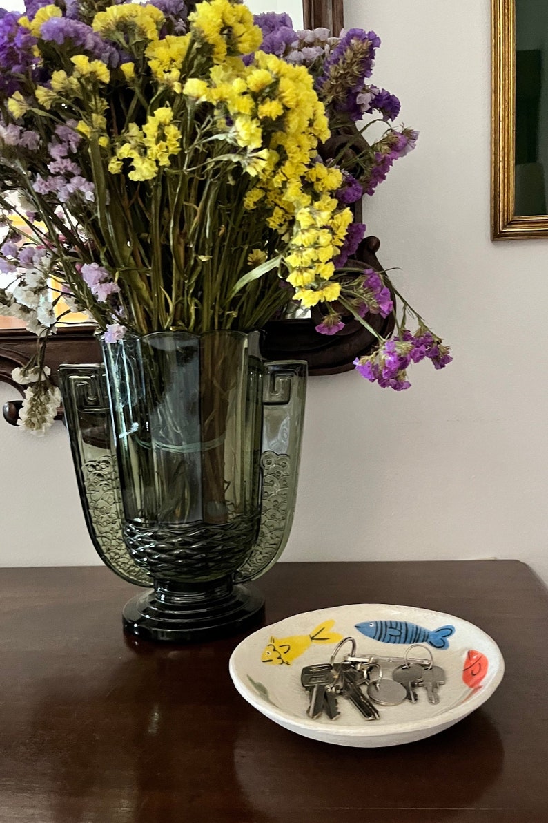 the bowl being used in a wooden table top with a glass vase with flowers on left side. The fish bowl has house keys on it.