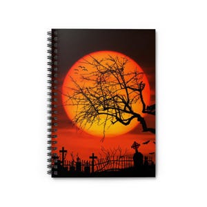 Könnte beinhalten: Ein gruseliges Halloween-Notizbuch mit einer schwarzen Silhouette eines Baumes vor einem großen orangefarbenen und roten Sonnenuntergang. Der Baum steht vor einem Friedhof mit einem Zaun und Kreuzen.