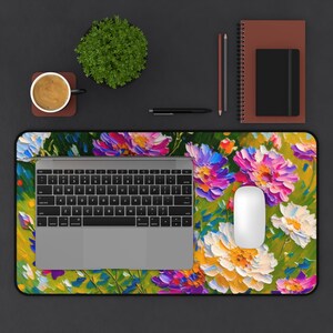 Könnte beinhalten: Schreibtischunterlage mit floralem Muster und einem lebendigen Design aus bunten Blumen in Rosa-, Lila-, Gelb- und Blautönen. Ein Laptop, eine Maus, eine Kaffeetasse, eine Pflanze und Schreibwaren sind auf einer dunklen Oberfläche angeordnet.