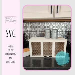May include: A white bread box with a wire mesh front. The bread box has a small handle on the front. The bread box is sitting on a counter with a metal backsplash. Two small metal canisters are sitting on top of the bread box.