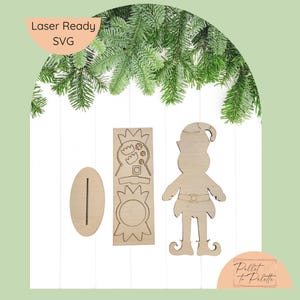 May include: Laser-ready SVG wooden Christmas elf and decorative pieces. The elf has a hat, belt, and curled shoes. The set includes an oval base with a slot and two decorative pieces. The text "Laser Ready SVG" is in the upper left.