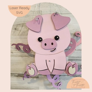 May include: Laser cut pink pig with a curled tail and a white heart on each foot. The pig is hanging from a string and has the text "Laser Ready SVG" and "Pillet to Palette" on the image.