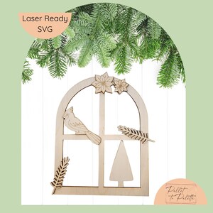 May include: A laser-ready SVG wooden cutout of a window with a cardinal, Christmas tree, and floral accents. The window is arched and has a natural wood finish. Green pine branches are at the top, and the background is white.