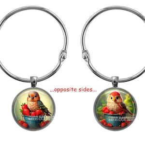 May include: A silver charm bracelet with two round glass charms. Each charm features a colorful illustration of a small bird sitting in a bowl of red strawberries. The text "Miss Dottie's" is visible on one of the charms.