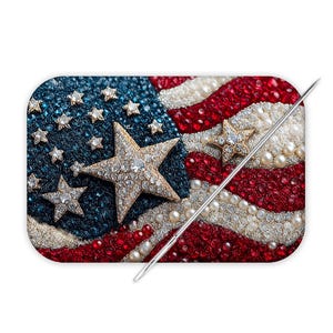 May include: A rectangular needle minder featuring a beaded and rhinestone American flag design with a blue field of stars and red and white stripes. A silver metal sewing needle is positioned diagonally across the surface of the flag.