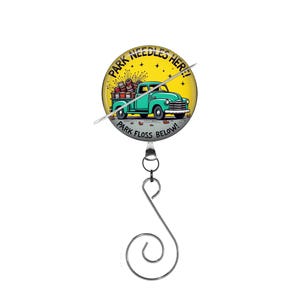 May include: A yellow and black circular badge with a blue pickup truck carrying a stack of colorful yarn balls. The badge reads "Park Needles Here! Park Floss Below!" and is attached to a silver retractable badge reel.