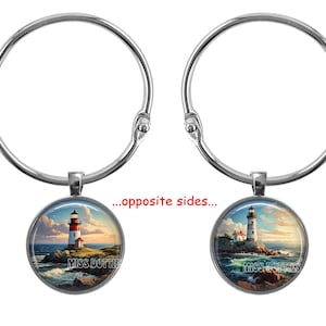 May include: A silver ring with a round glass charm featuring a lighthouse on a rocky shore with blue water and a cloudy sky. The charm has the text "Miss Lottie's" on it.