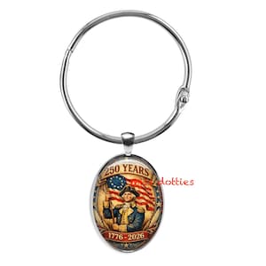 May include: A silver-colored metal ring with an oval pendant. The pendant features an illustration of a man holding a flag with the text "250 YEARS 1776-2026". The flag has red and white stripes and stars.