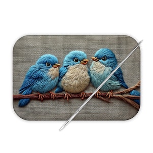 May include: Embroidered artwork featuring three bluebirds perched on a brown branch. The birds have blue feathers, tan chests, and orange beaks. The background is a textured gray fabric. A needle is placed diagonally across the image.