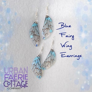 May include: Blue fairy wing earrings with a silver hook and a clear, iridescent wing design with blue accents. The wings have a delicate, intricate pattern and are accented with small blue flowers.
