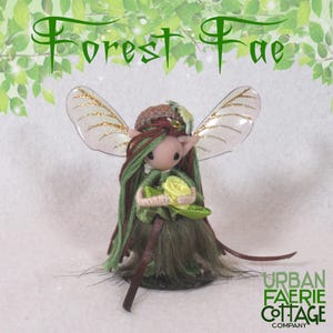 May include: A set of three ceramic mugs with a speckled, cream-colored glaze. Each mug features a different hand-painted design: a blue and green leaf, a yellow sun, and a pink flower. The mugs have a simple, modern design.