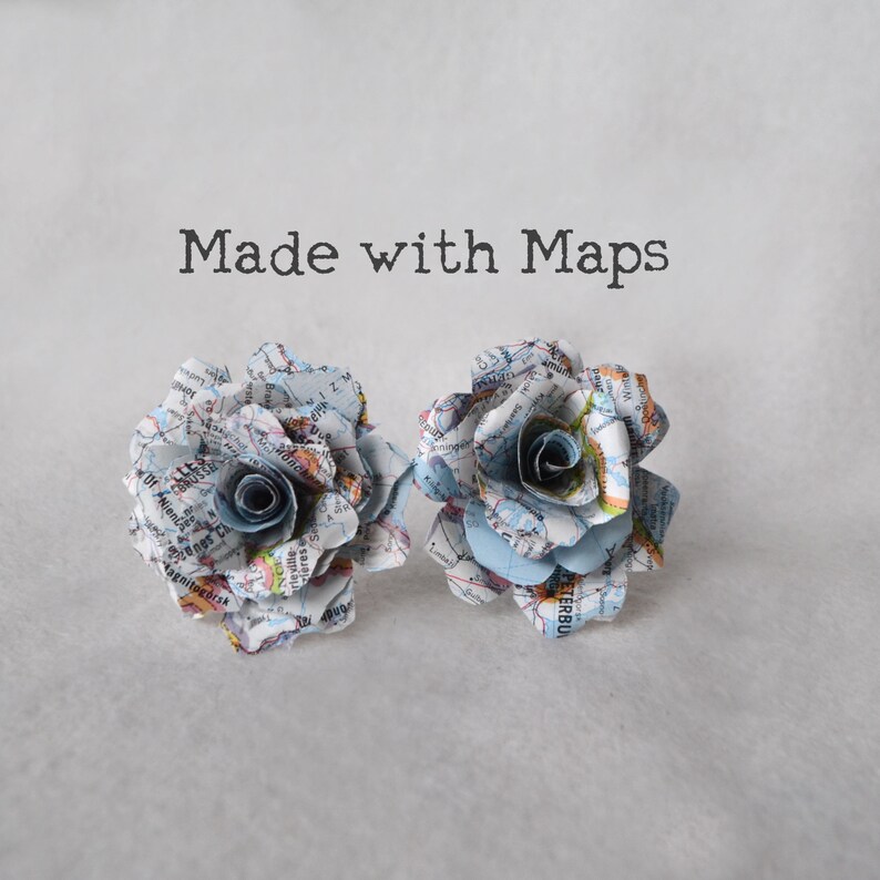 Puede incluir: Dos rosas de papel hechas con mapas antiguos. Las rosas son de color azul claro y blanco con un centro gris claro. El texto "Made with Maps" est&aacute; por encima de las rosas.