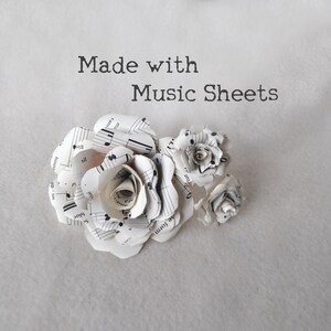 Puede incluir: Tres rosas blancas de papel hechas con partituras. Las rosas est&aacute;n dispuestas en un racimo. El texto "Made with Music Sheets" est&aacute; escrito sobre las rosas.