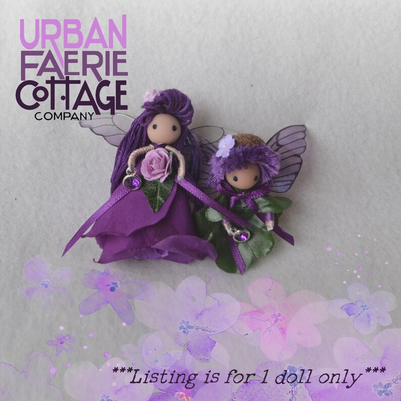 May include: Two purple fairy dolls with wings and flowers. The dolls are made of wood and fabric. The text "Listing is for 1 doll only" is at the bottom of the image.