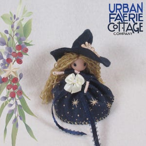May include: A small witch doll with blonde yarn hair, wearing a navy blue dress with gold stars and a black witch hat with gold trim. The doll is holding a gold wand with a star charm.