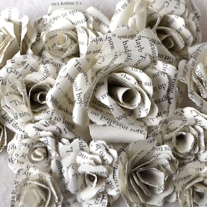 Puede incluir: Un primer plano de un ramo de flores de papel hechas con p&aacute;ginas de libros. Las flores est&aacute;n dispuestas en forma circular y son todas blancas. El texto en las p&aacute;ginas es visible, creando un aspecto &uacute;nico y texturizado.