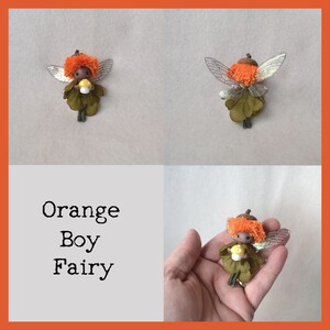 Op de afbeelding: Oranje jongensfeepop met bruine huid, oranje haar en groene vleugels die een gele paddenstoel vasthouden. De fee is gemaakt van stof en heeft een houten hoofd.