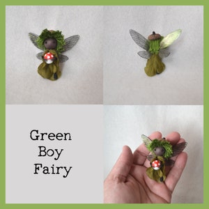 Op de afbeelding: Groene jongen fee figuur met vleugels, die een rode en witte paddenstoel vasthoudt. De fee draagt een groene en bruine outfit en heeft een groen mossig hoofd.