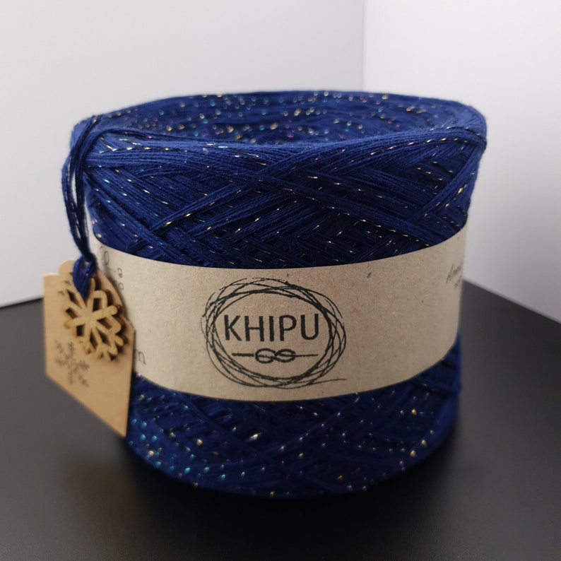 May include: A skein of dark blue yarn with iridescent glitter threads. The yarn is wrapped around a cardboard tube with a brown paper label that says "KHIPU" with a knotted rope design.
