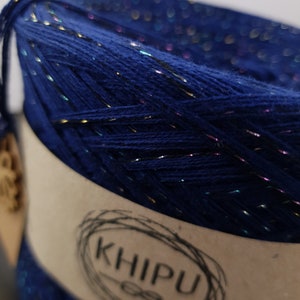 May include: A skein of dark blue yarn with iridescent glitter threads. The yarn is wrapped around a cardboard tube with a label that reads "KHIPU".