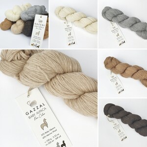 May include: Assortment of yarn skeins in various colours, including grey, brown, and beige. The yarn is labelled "GAZZAL BABY ALPACA Pure Colour" and includes the yarn composition and yardage.
