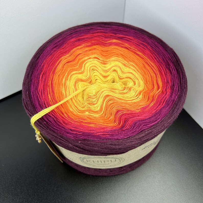 May include: A skein of yarn in a gradient of colors from deep purple to yellow. The yarn is wound into a ball and the label reads "KHIPU".