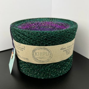 May include: A skein of green yarn with silver glitter, wound on a cardboard spool. The yarn is labeled "Khipu" and "Anna Sakowska".
