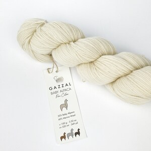 May include: A skein of cream-coloured yarn labelled "GAZZAL BABY ALPACA Pure Colors" with a label that reads "55% Baby Alpaca 45% Merino Wool  ~100 g - 3.52 oz  ca 320 mt - 349 yd".